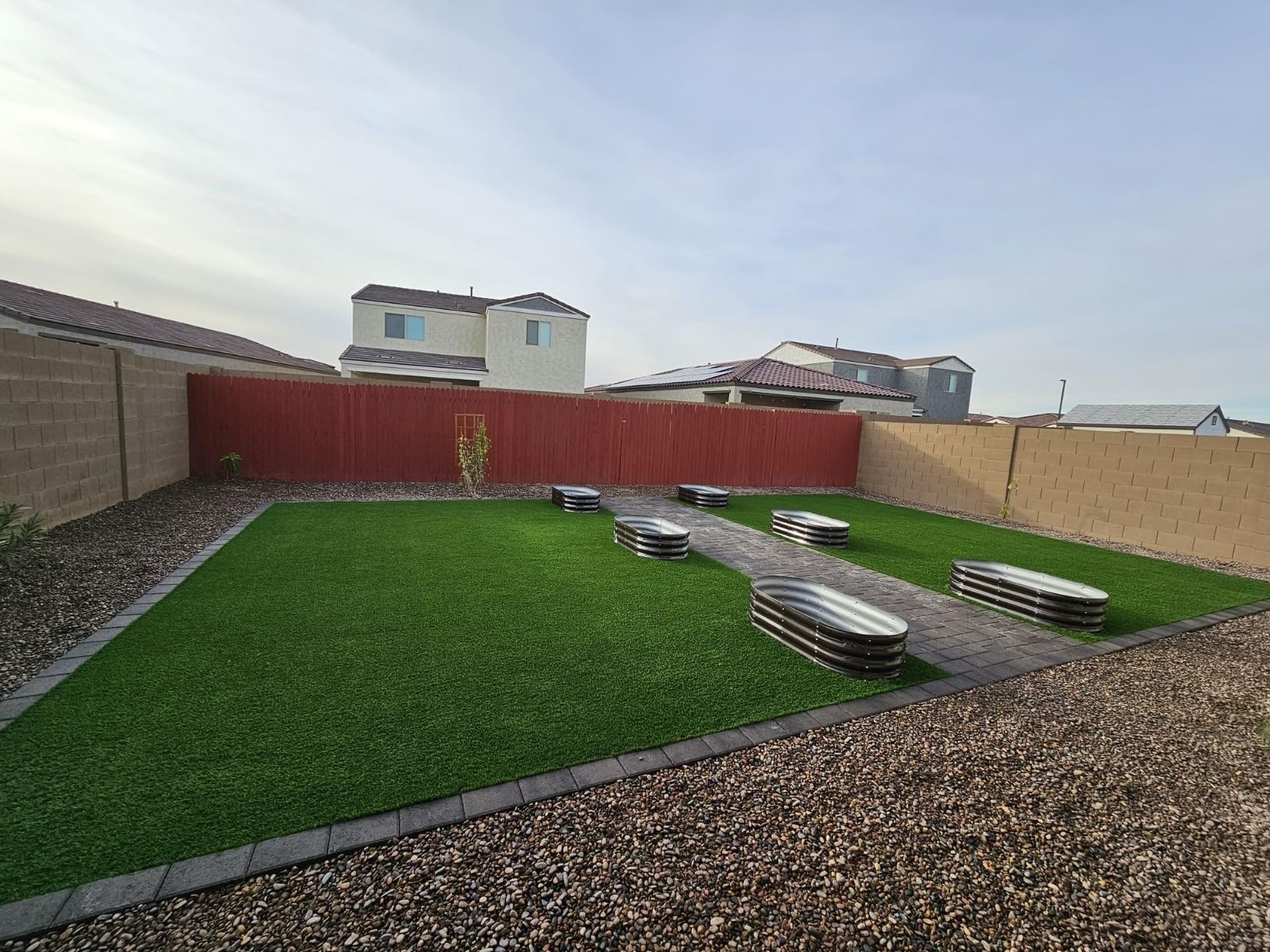 Metal raised garden beds on artificial turf in a backyard with gravel and red fence