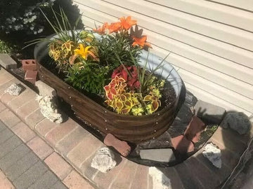 Wooden raised garden bed with colorful flowers, set on brick patio near house siding