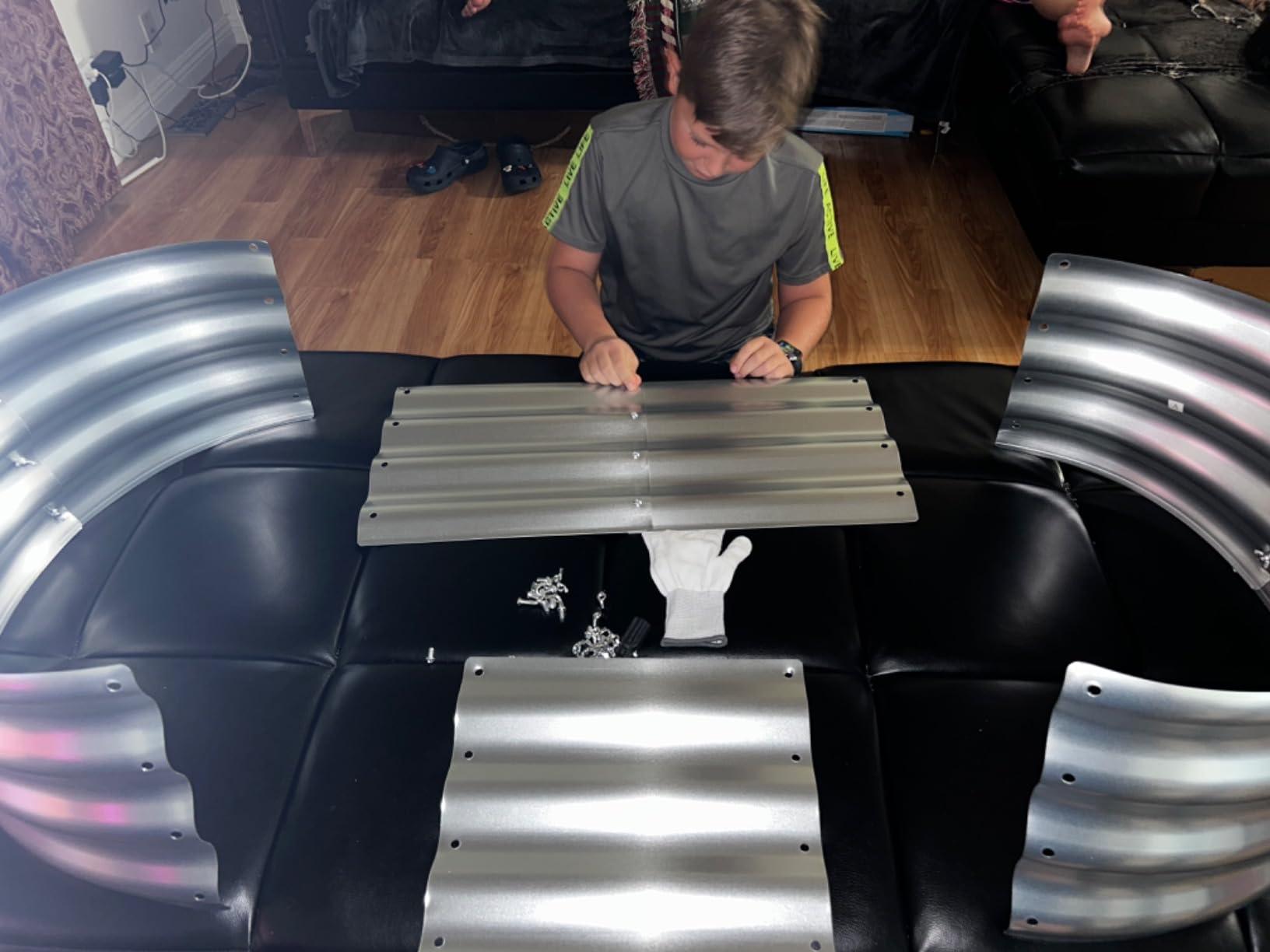 Boy assembling metal raised garden bed panels on couch, DIY garden kit parts laid out