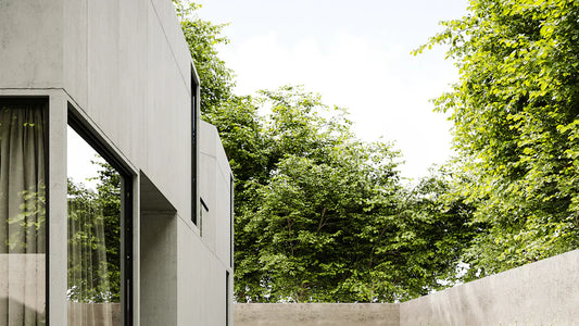 Modern concrete home exterior with large windows and lush green trees in backyard garden setting