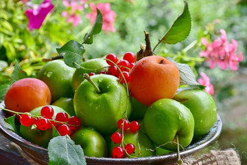 Fresh green apples, red currants, and apricots in a rustic bowl with garden blooms