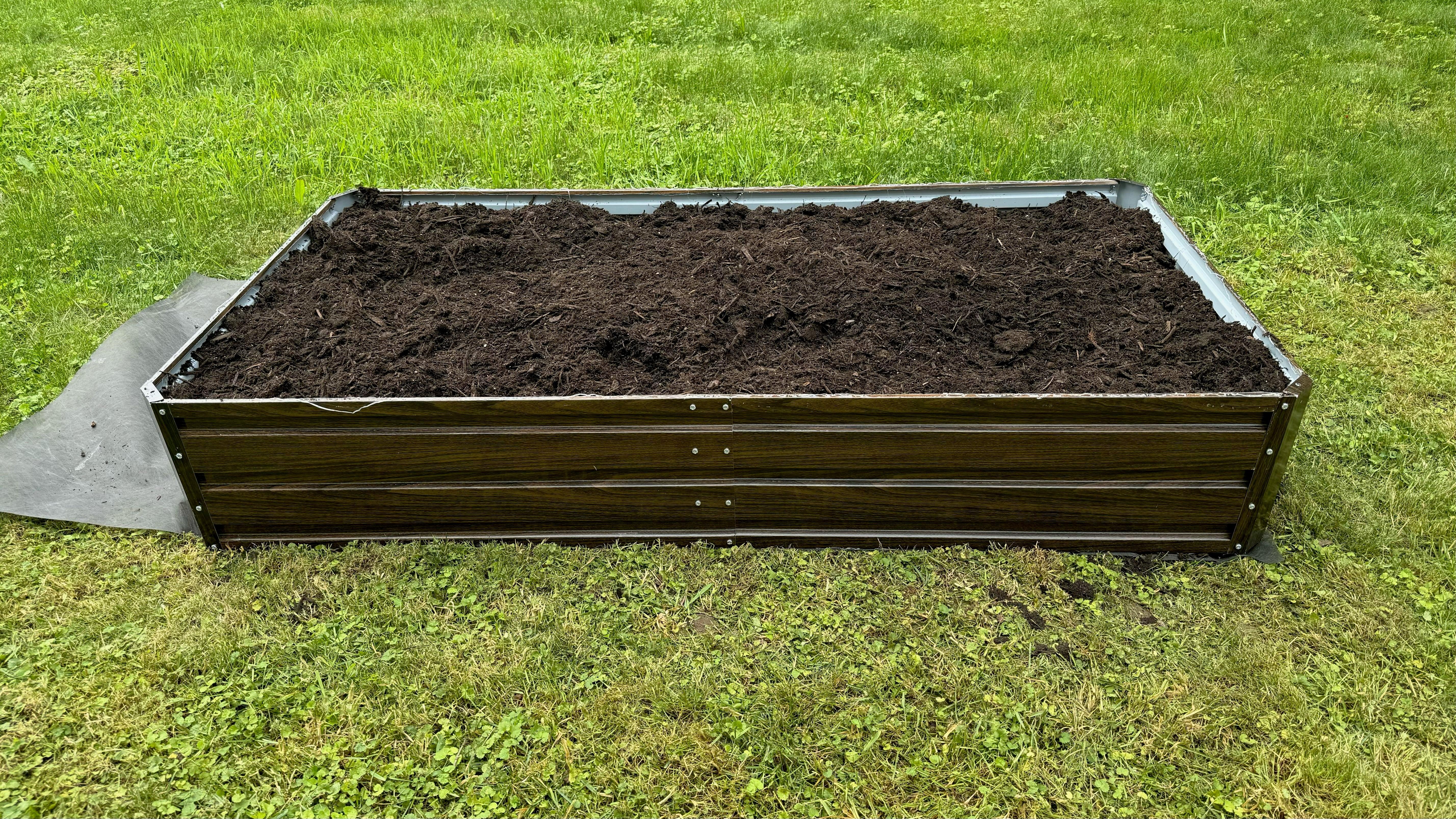 Metal raised garden bed filled with soil, set on green grass for outdoor gardening.