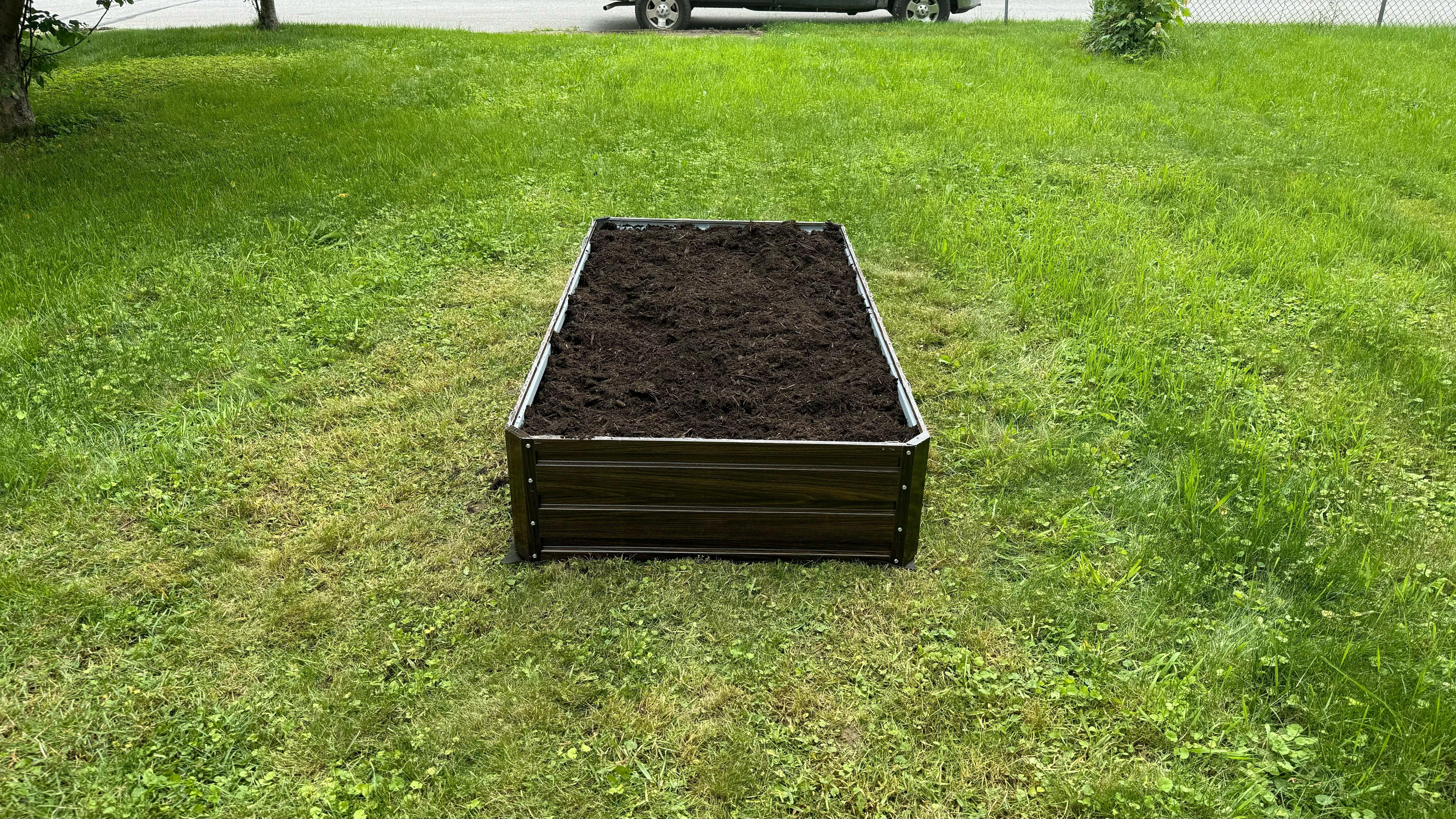 Metal raised garden bed filled with soil, placed on a lush green lawn for backyard gardening.