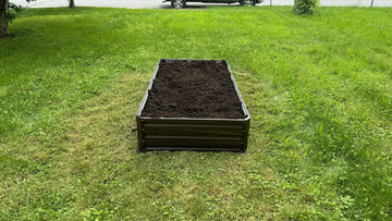 Metal raised garden bed filled with soil, placed on a lush green lawn for backyard gardening.