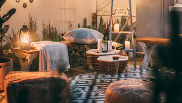 Cozy outdoor patio setup with wooden furniture, lantern, wine, and string lights for evening relaxation