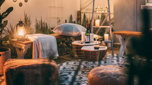 Cozy outdoor patio setup with wooden furniture, lantern, wine, and string lights for evening relaxation