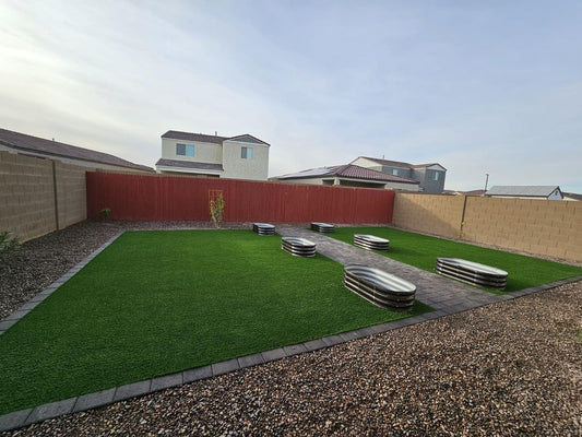 Metal raised garden beds on artificial turf in a backyard with gravel and pavers